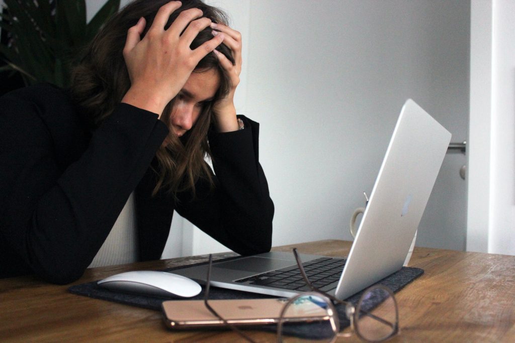 Woman holding her head in frustration while looking at a laptop